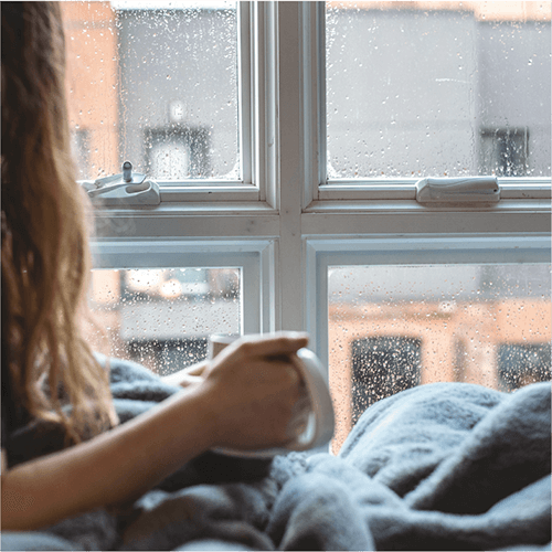 雨が降る窓の外を眺める女性の写真
